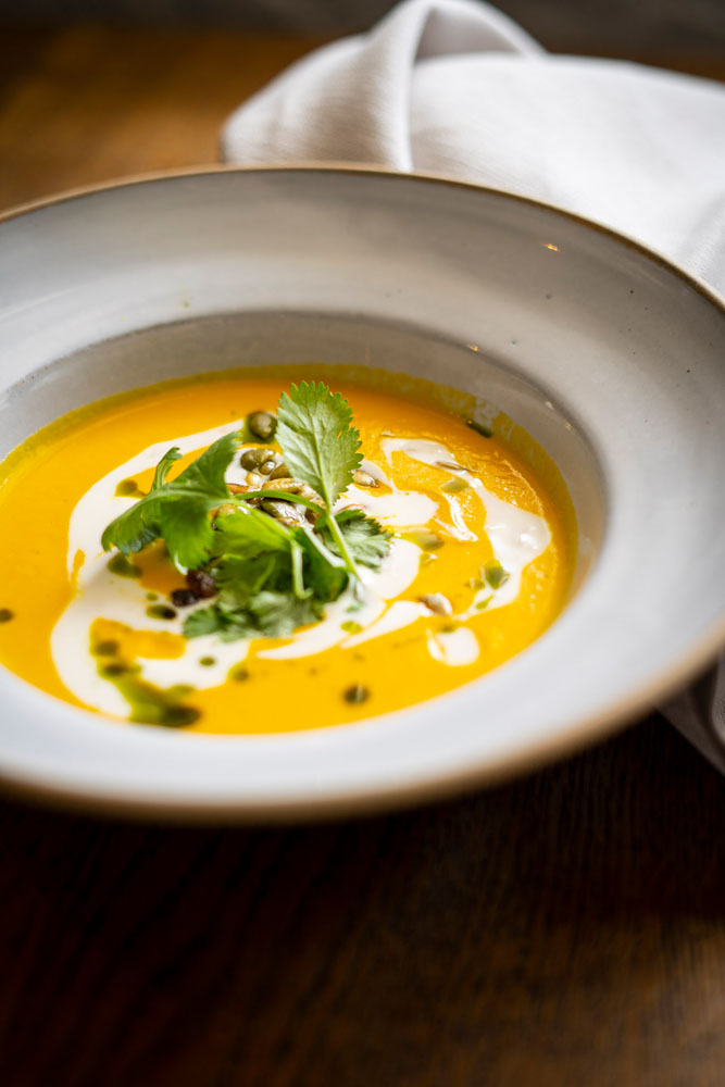 An orange soup with greens on a fancy plate