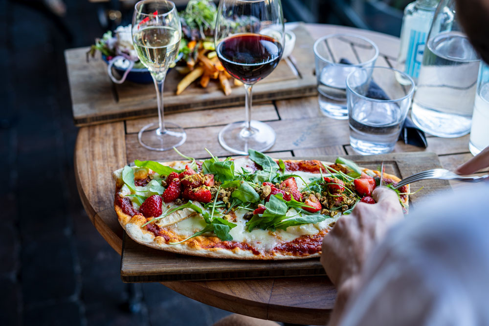 A table with a fancy pizza, and a glass of red wine