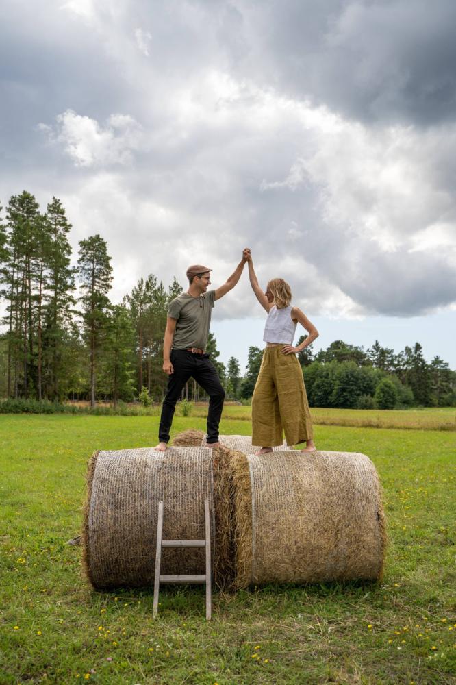 A man and woman standing on top of hay bales in a field.
