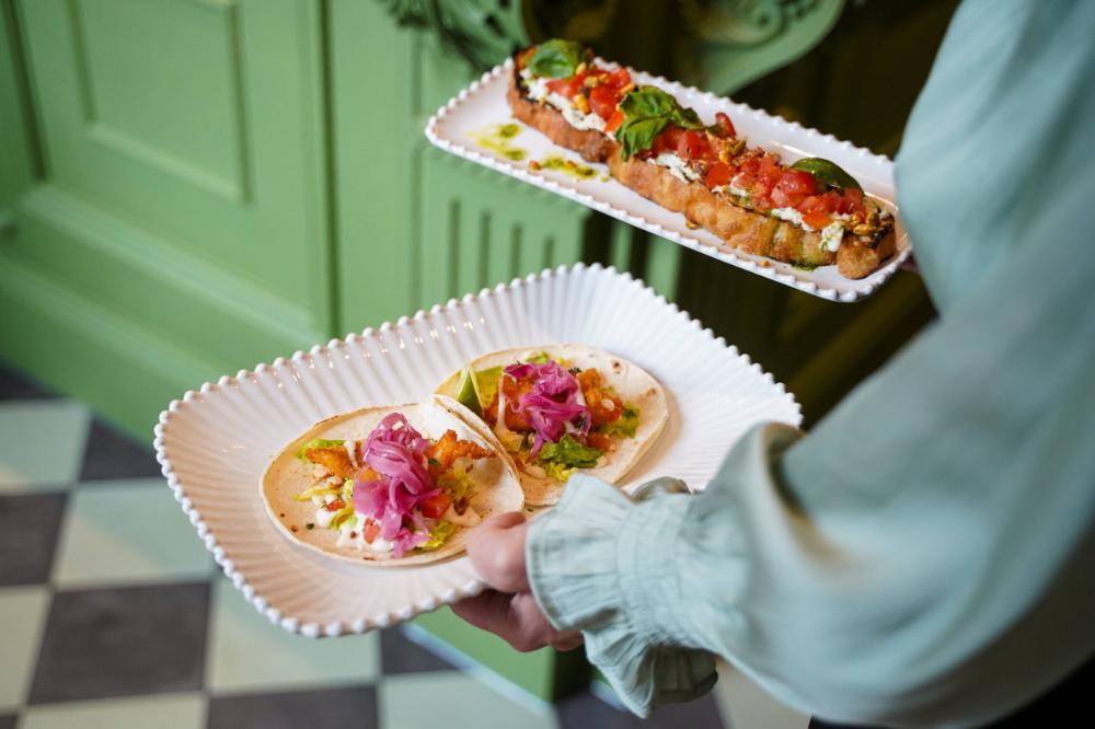 A woman is holding two plates with tacos on them.