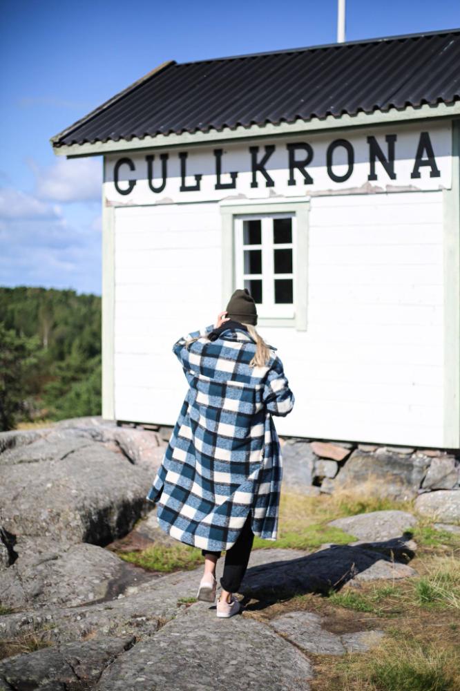 A woman in a plaid coat is standing in front of a house.