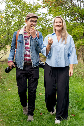 Linda and a friend walk on grass eating apples.